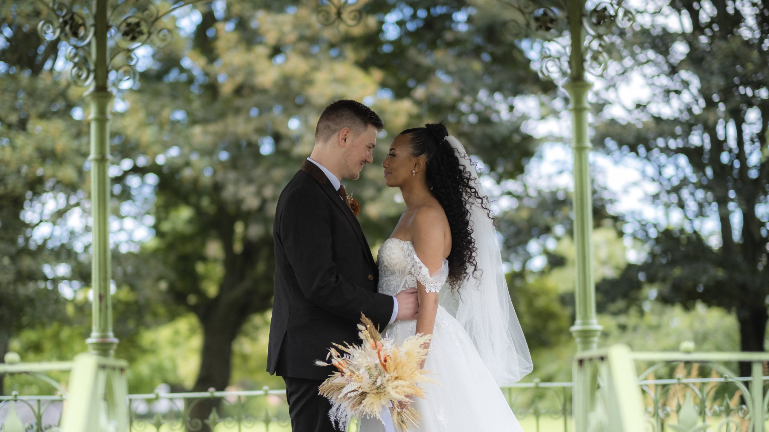 Bride and groom facing each other under a green bandstand