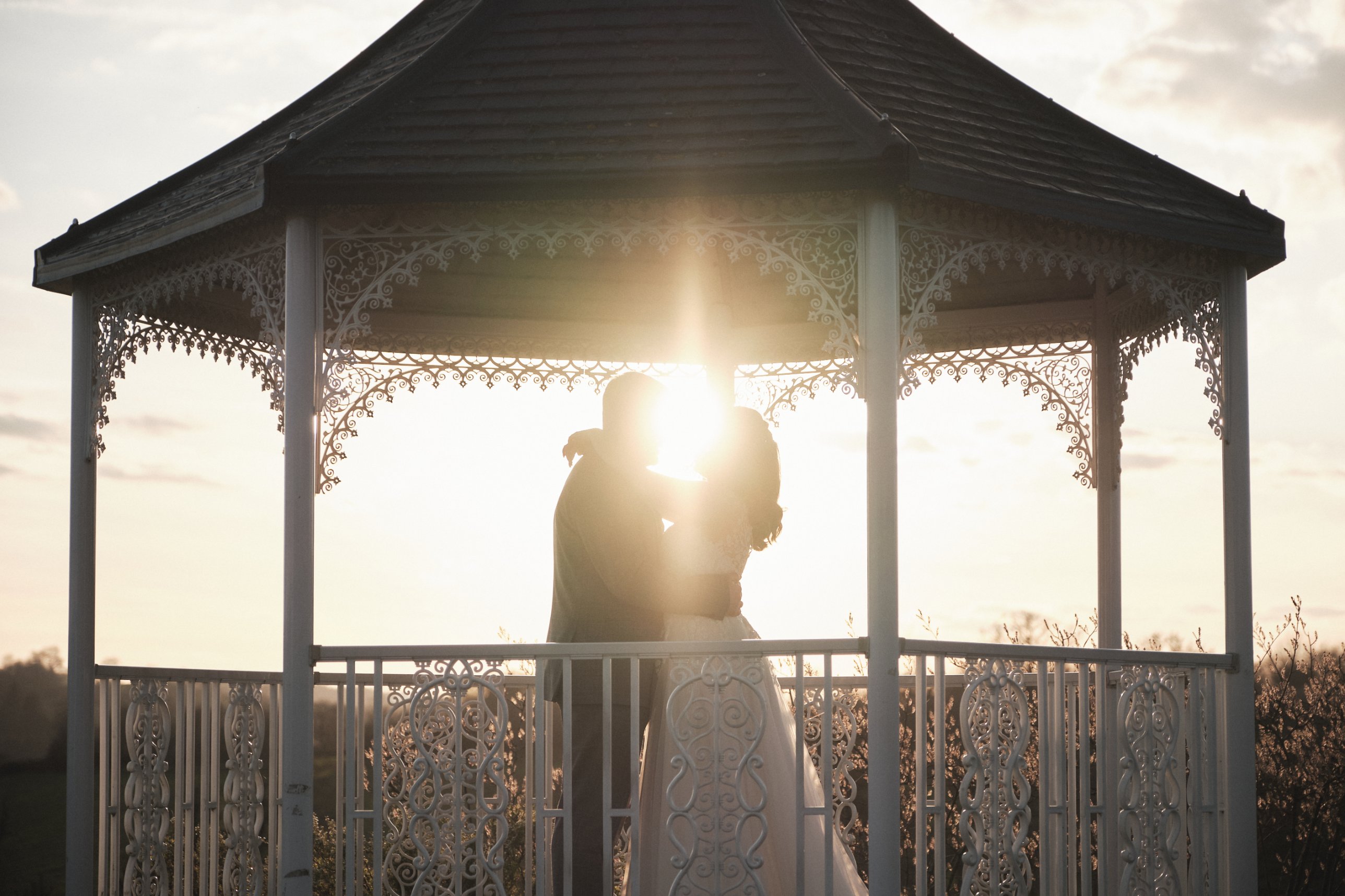 Couple silhouetted inside a white gazebo at sunset