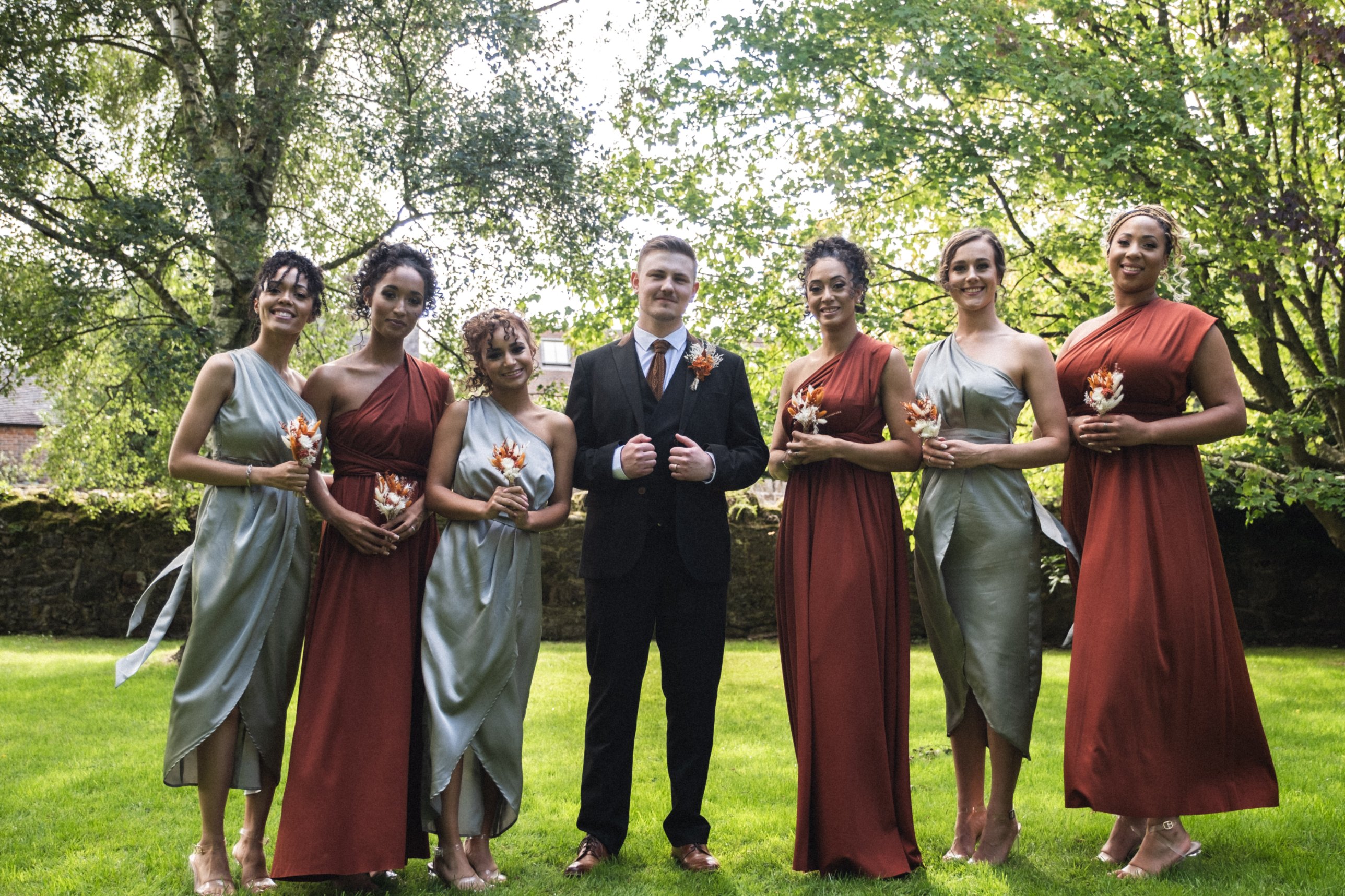 Groom with six bridesmaids in rust and sage dresses