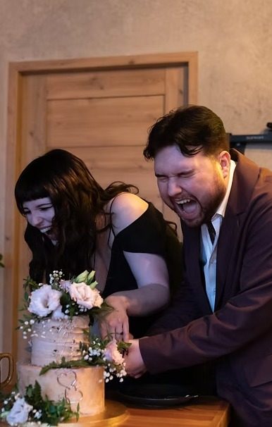 Zuzia and Ben laughing as they cut their wedding cake